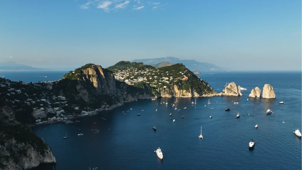 Aerial view of Capri’s coast and the Faraglioni, with boats on the sea